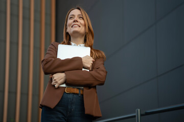 Woman smiling looking up holding laptop outdoors