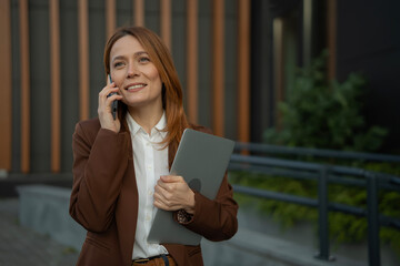Confident businesswoman communicating on smartphone holding laptop