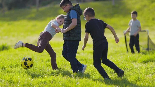 Children playing soccer and dribbling ball in sunny park