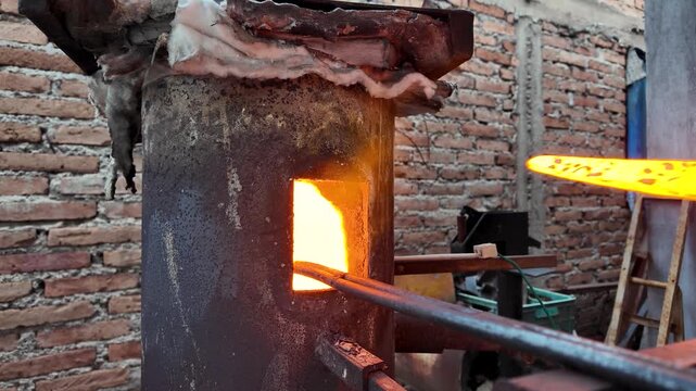 Artisan blacksmith removing a glowing red-hot steel knife blade from the forge furnace.