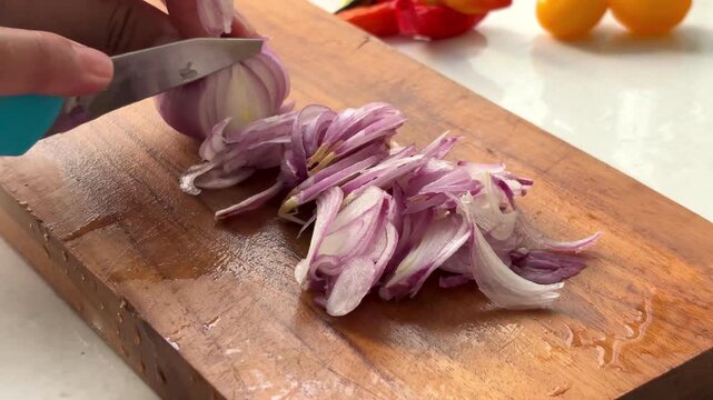 Woman hands slicing shallots thinly on wooden cutting board for cooking. Kitchen preparation scene ideal for searches like chopping onions and food preparation.