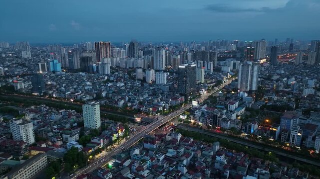 Wide aerial panorama of Hanoi at dusk featuring intersection of Tran Duy Hung and Lang Street, dense housing, linear traffic flow, and expanding urban skyline.