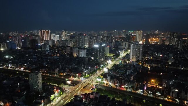 Night aerial view over Hanoi showing Tran Duy Hung and Lang Street intersection with bright traffic streams, dense neighborhoods, and glowing skyline under dark sky.