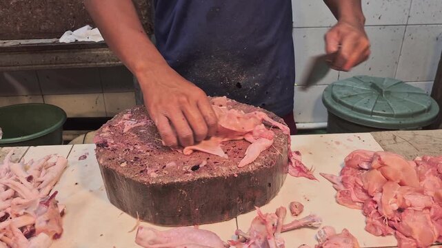 Close-up video of a butcher's hands cutting up fresh raw chicken using a heavy meat cleaver on a simple wooden block in a traditional wet market.