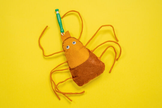 Plush toy tick with a green pet tick remover attached on a bright yellow background creating a humorous concept about protecting animals from ticks and parasites