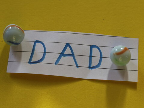 Una toma de cerca de la palabra padre en un papel blanco rodeado de canicas o metras en un fondo Amarillo para ser utilizado el d&iacute;a del padre