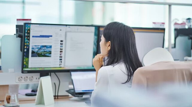 Professional woman focused on her work at a modern office desk with multiple computer monitors, demonstrating dedication and productivity in a corporate environment.