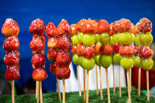 Candied strawberries and green grapes on skewers with glossy sugar coating, colorful street food dessert close up
