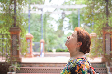 Senior latin woman enjoying a summer afternoon outdoors in a park, Rosedal de Palermo, in Buenos Aires, Argentina. A profile portrait in which she is looking up, framed with copy space. © Carolina Jaramillo