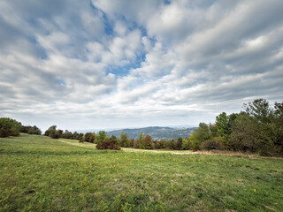 Obraz premium Panoramic pasture landscape on Vrh Rajac in Serbia, with open meadow, distant hills and dramatic cloud cover above a rural highland scene in the Rajac mountain area.