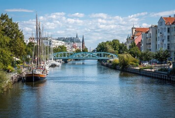 Fototapeta premium Sailboat on River View with Bridge and Buildings, Daytime