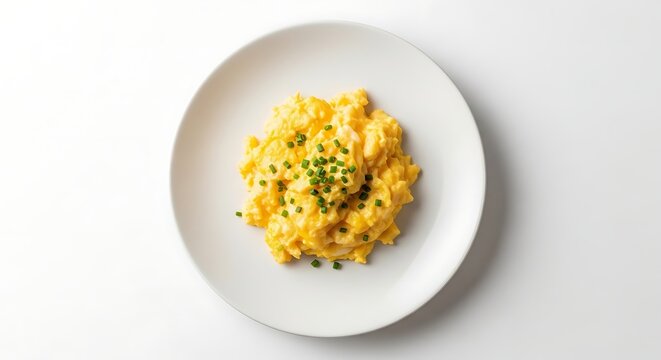 A top-down view of fluffy scrambled eggs garnished with chopped chives on a white plate