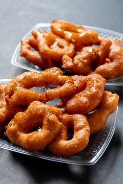 Picarones peruanos: postre tradicional de masa de camote y zapallo con miel de chancaca sobre fondo gris.