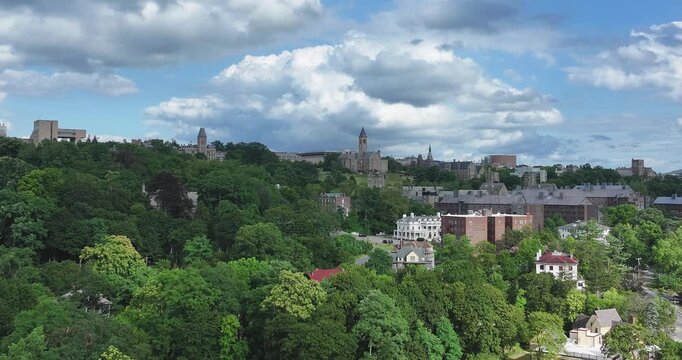 Stunning video captures a vibrant university campus, where historic architecture meets lush, rolling hills. The dense, emerald canopy of trees frames the scene, all under a dynamic sky. 