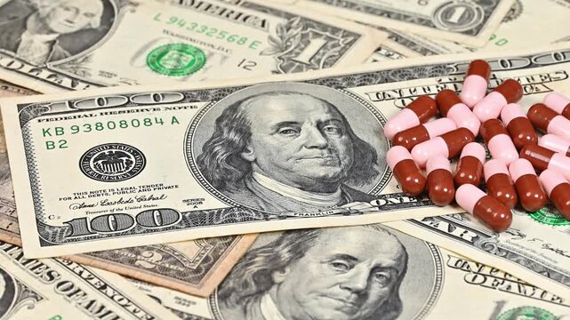 One hundred dollar bills with medical capsules, pharmaceutical cost concept and cash
