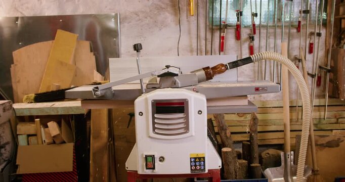 Carpenter occupation. Joinery equipment. Man starting lumber processing in furniture workshop guiding wooden board in thickness planer.