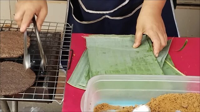 The preparing "Khao Puk Gya," a traditional northern Thai pancake made with black sesame seeds, sprinkled with palm sugar, and wrapped in banana leaves, requires care and expertise.
