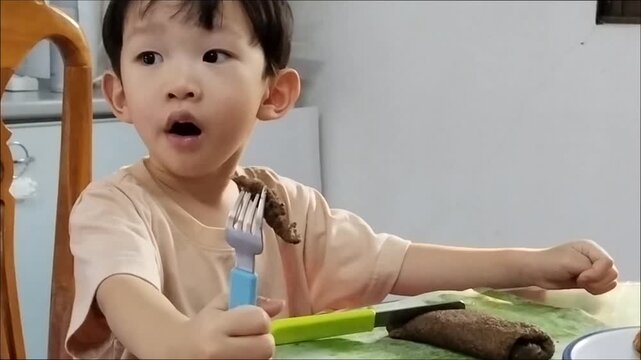 An Asian child is eating "Khao Puk Gya" a traditional northern pancake made with black sesame seeds, sprinkled with palm sugar, and wrapped in banana leaves