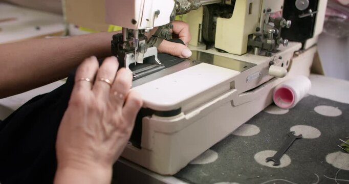 Clothing making. Sewing process. Tailor hand working on stitching professional machine. Woman creating buttonhole on black fabric.