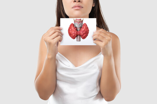 A young woman holds an image of the thyroid gland in front of her neck, representing thyroid cancer, symptoms, diagnosis, and possible complications in a clean minimal background. thyroid cancer. thyr