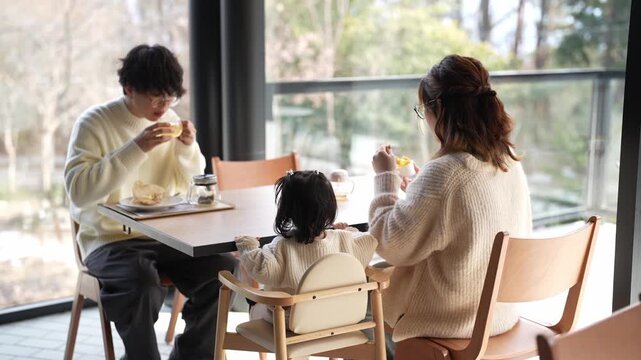 Cozy family dining by large window. Soft light, warm tones, calm atmosphere. Mother and father smile gently, child eats happily. Ideal for family lifestyle, daily routine, or comfort themes