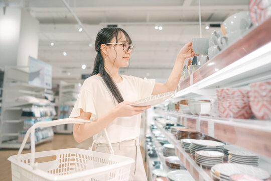 Smiling asian woman shopping choosing plate product for home at indoors japan style warehouse superstore