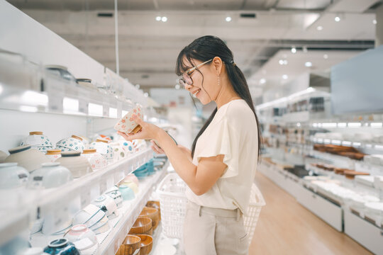 Smiling asian woman shopping choosing plate product for home at indoors japan style warehouse superstore