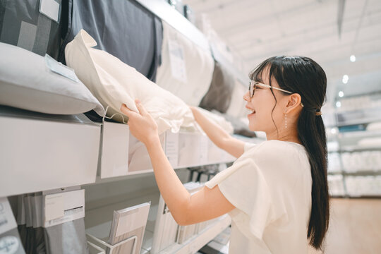 Smiling asian woman shopping choosing bed pillow product for home at indoors japan style warehouse superstore