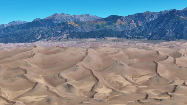 Panoramic view of Great Sand Dunes National Park in Colorado's landscapes with stunning aerial views of mountains and fall foliage during morning sunrise light in autumn season - 4K Drone