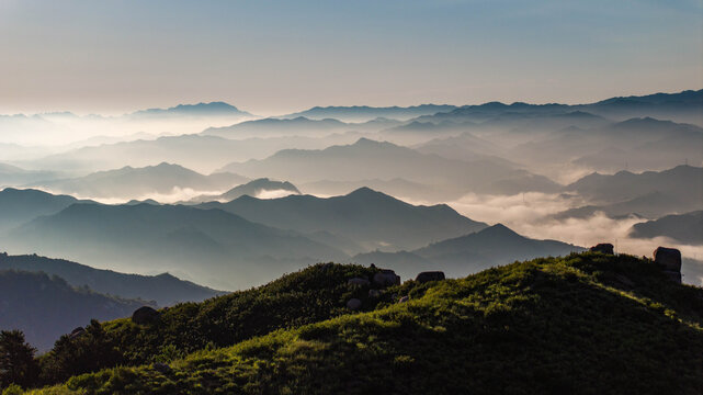 Layered mountain ranges covered by a sea of clouds at sunrise in northern China. Warm golden light illuminates drifting mist between ridgelines, creating depth and atmospheric perspective.