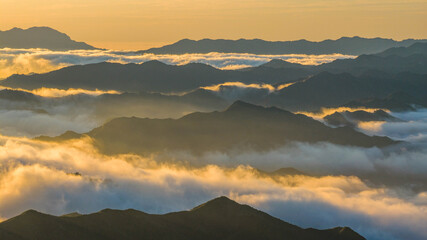 Layered mountain ranges covered by a sea of clouds at sunrise in northern China. Warm golden light illuminates drifting mist between ridgelines, creating depth and atmospheric perspective. © Isabel