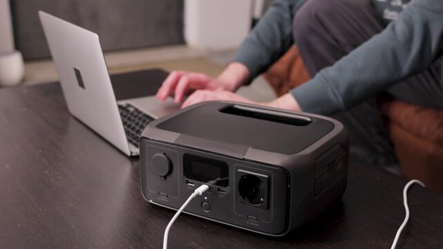 Portable power station on a table with a person working on a laptop in the background. Modern energy solution for home office or off-grid power.
