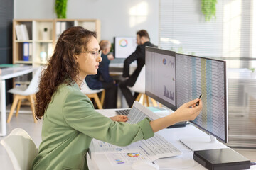 Analyst woman at computer reviewing budget data. She compares spreadsheet columns on dual screens. Accounting control enables timely reporting. Accuracy and productivity office concept.