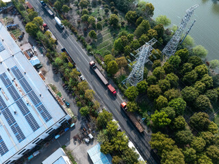 Fototapeta premium Aerial view of industrial area with trucks on road, high-voltage transmission towers, greenery and solar panels on factory roof