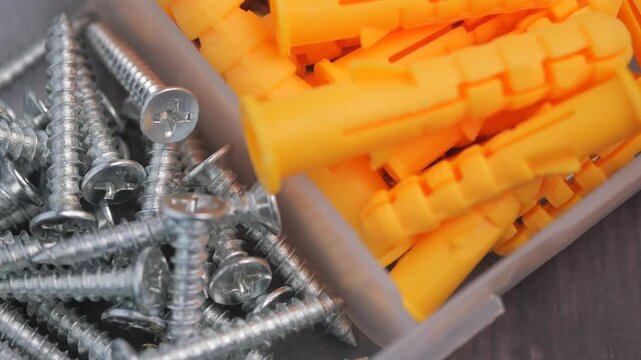 Hardware for home improvement self-tapping screws and plastic dowels in small box close up.