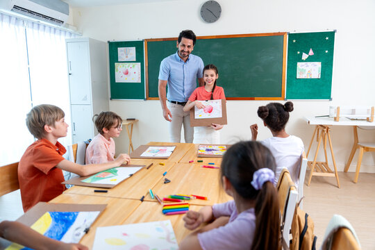 Wide shot of the teacher encorage lovely girl to present his painting also explain the meaning of it in front of the classroom and friends also interest in his creation.