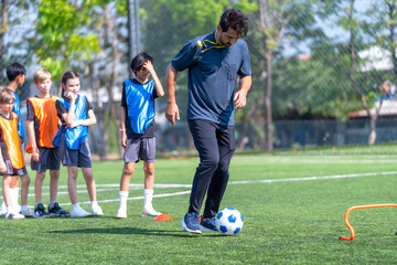 Fototapeta premium Coach show and guide the children to dribble the ball pass through obstacle in the field to practice and prepare for the competition.