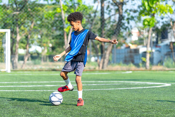 Obraz premium A little african-american boy is dribbling the football in the field to play soccer alone during day light to practice and prepare for competitiion.