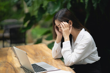 Stressed young professional woman sitting at a wooden desk with laptop in a serene green environment, feeling overwhelmed by workload and pressure