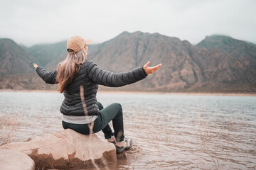 Woman in puffer jacket and cap enjoying a foggy mountain lake view © Jezabel
