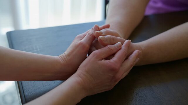 Close up footage of Granddaughter gently holding her Grandmother hands across a table, expressing love, care, family support, and intergenerational connection.
