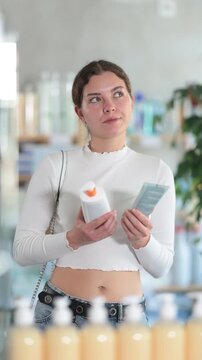 Girl in summer clothes choosing skin cream at the drugstore. High quality 4k footage