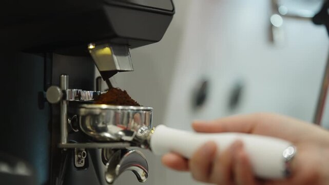 Close-up sequence of a barista grinding fresh coffee into a stainless portafilter with a commercial espresso grinder, demonstrating precise dosing and preparation in a modern cafe before brewing