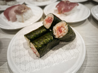 Fresh tuna maki sushi rolls wrapped in crispy nori seaweed, served on a white patterned ceramic plate in a Japanese restaurant © catinsyrup