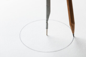 Drafting compass drawing circle on white paper background macro.