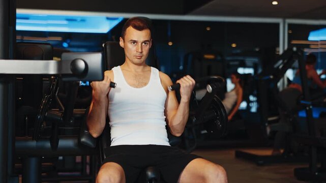 Determined young guy training his forearms using arm curl machine in fitness hall