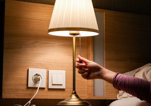 Woman hand turning on or turning off switch the minimal lamp in modern bedroom. warm cozy lighting with wooden interior, night ambient. comfort and relaxation. Apartment living concept.
