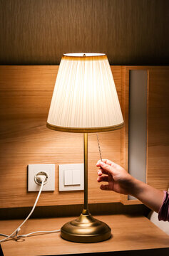 Woman hand turning on or turning off switch the minimal lamp in modern bedroom. warm cozy lighting with wooden interior, night ambient. comfort and relaxation. Apartment living concept.