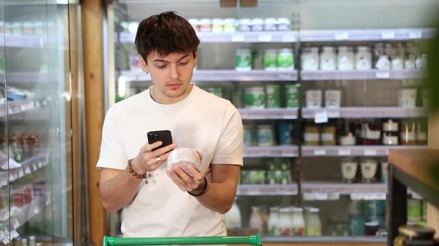 European guy scans a mobile barcode of a cheese package in an eco supermarket. Customer pays online for purchases in an organic store with farm products. High quality 4k footage