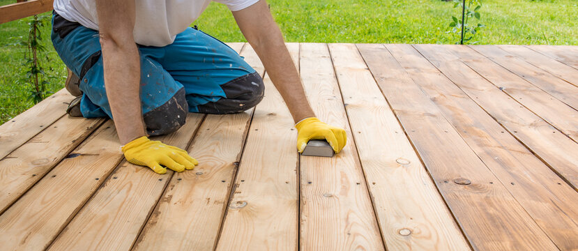 Worker kneels on wooden deck, sanding planks